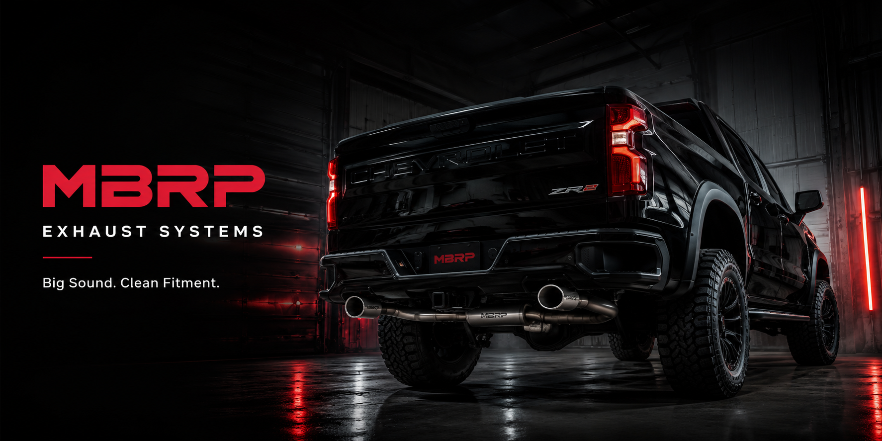 Black Chevrolet truck with MBRP exhaust system in a dark garage showing dual exhaust tips and red performance lighting